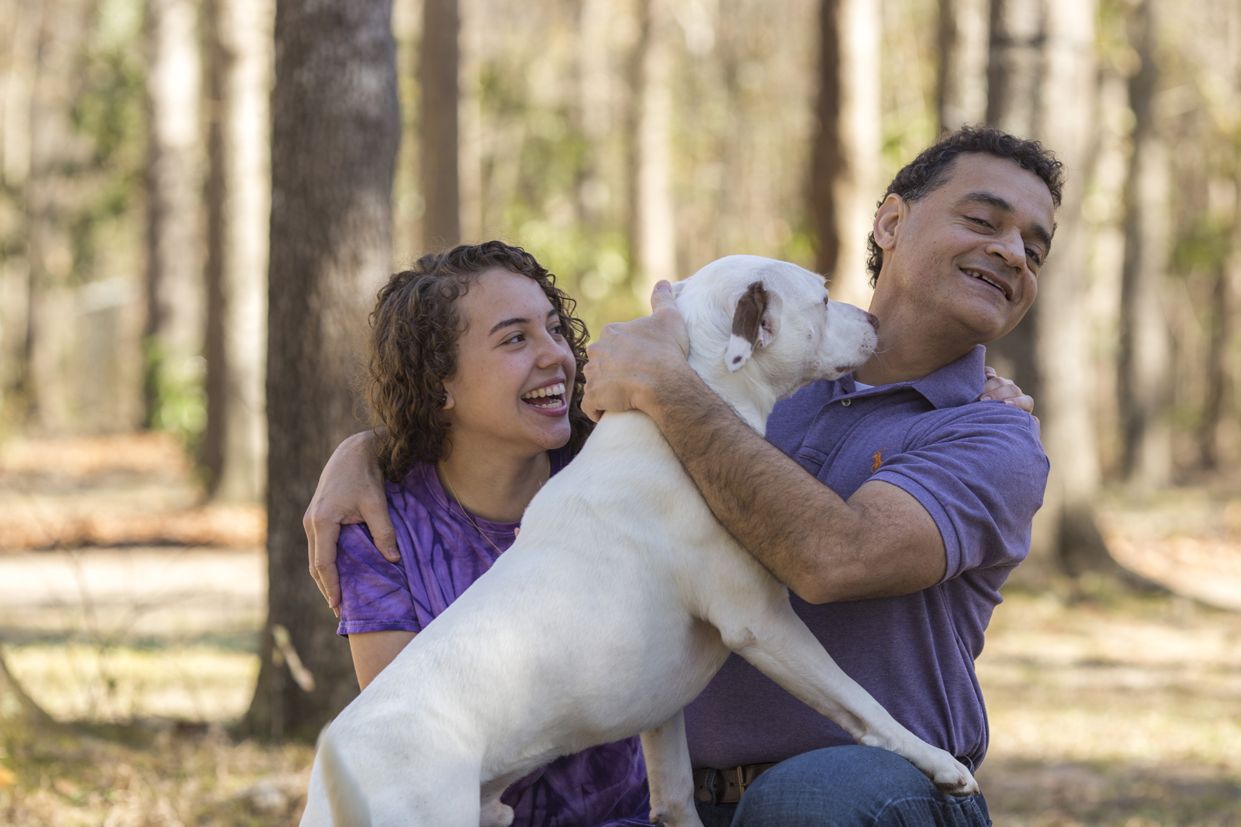medium sized white dog licks dad's face as teen girl laughs.