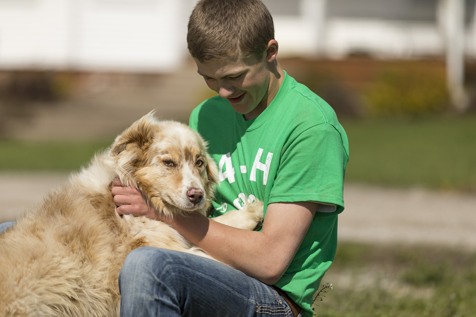 teen boy wearing 4-H t-shirt kneels next to and talks to dog.
