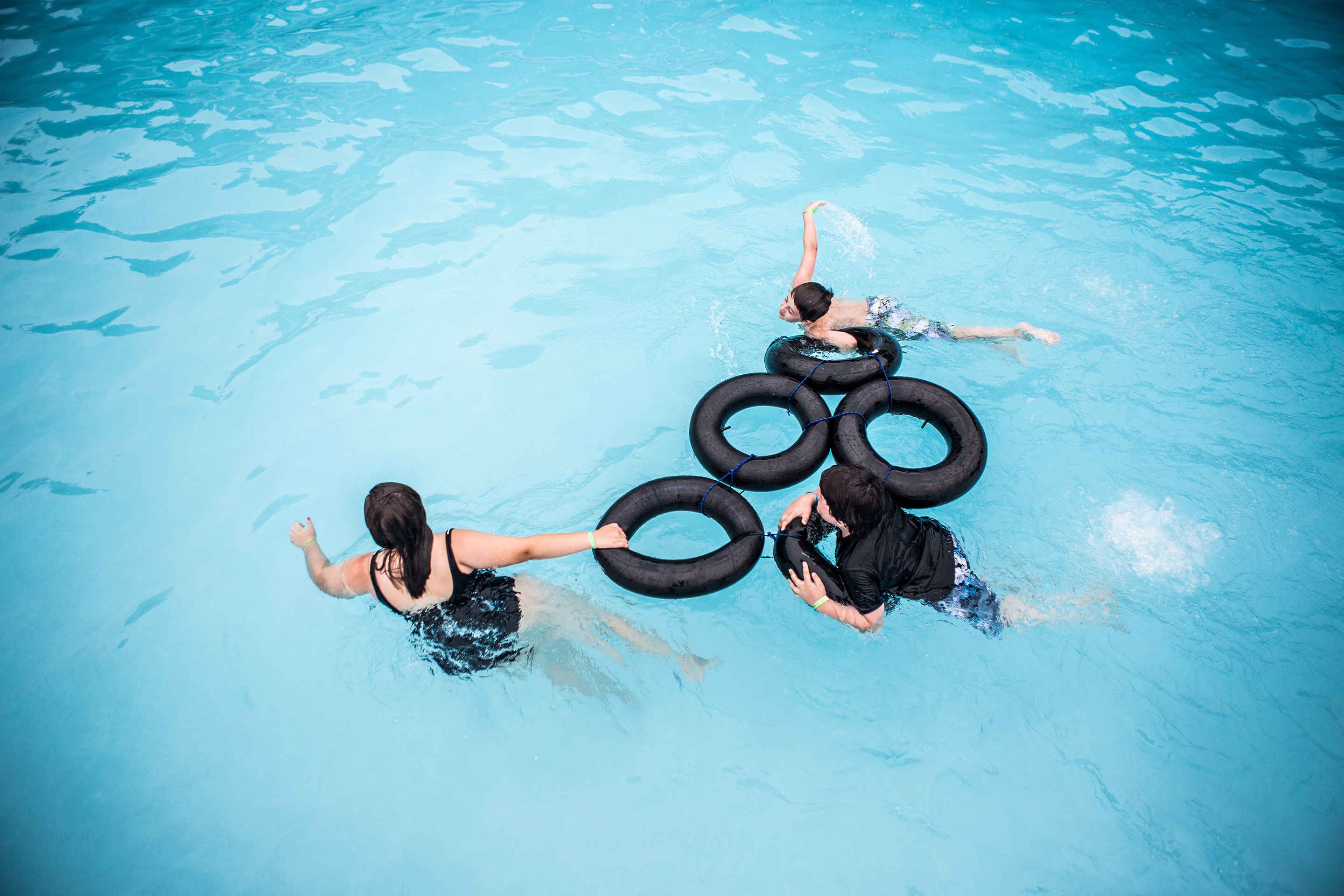 girls hold onto flotation device as they swim through pool
