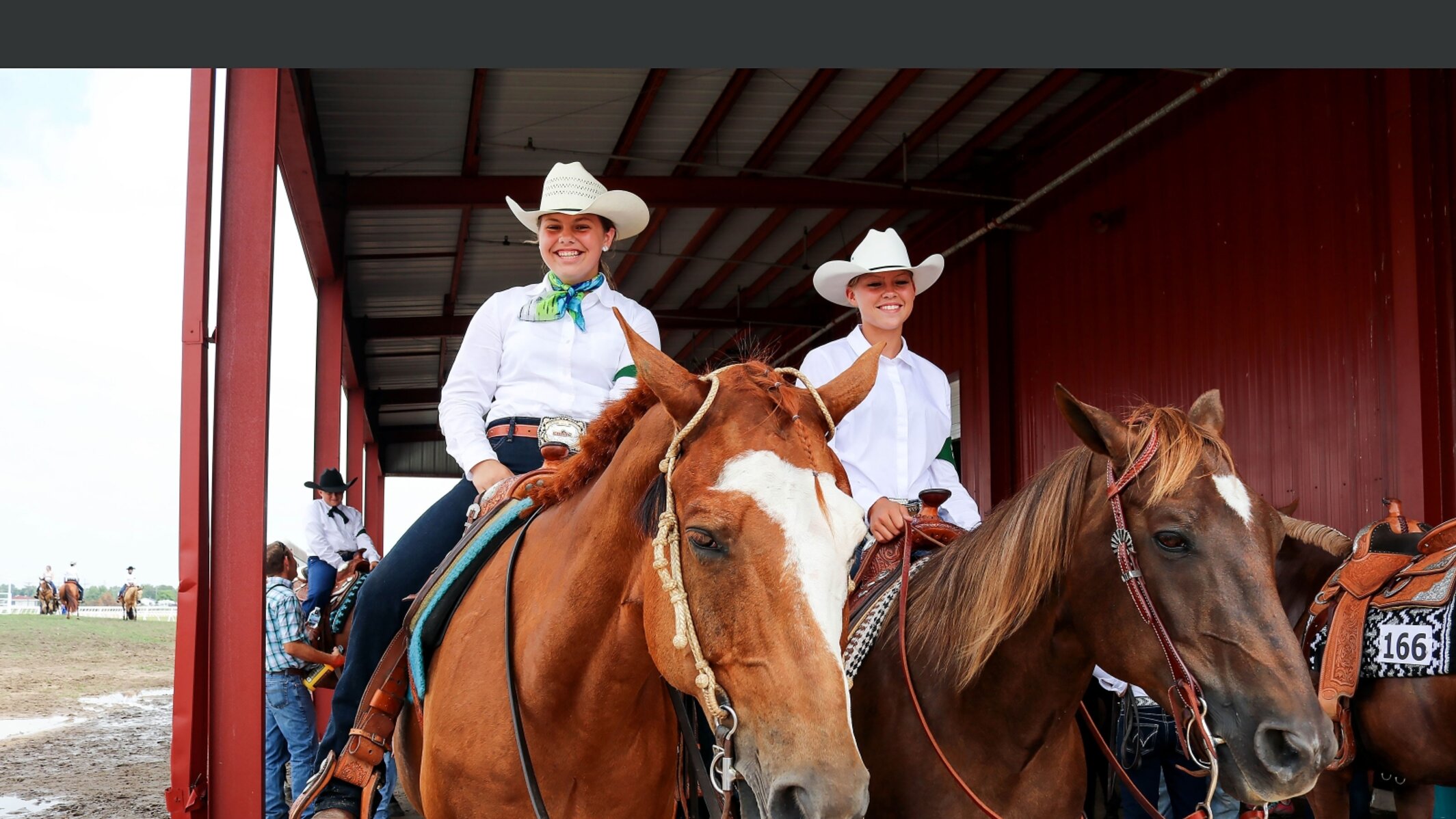 Two girls in show dress sit smiling next to each other on their horses
