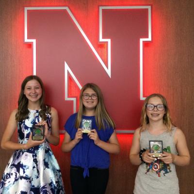 three 4-H members stand with their awards in front of glowing Nebraska N