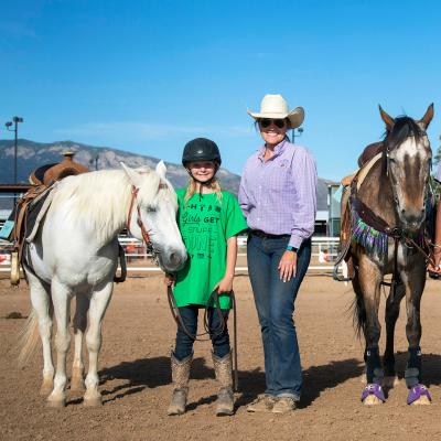 4-H volunteer leader smiles as she stands next to members and their horses