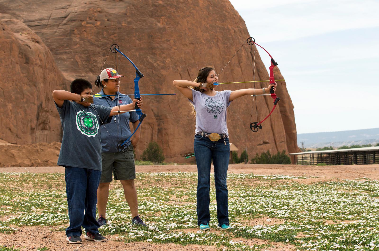 shooting sports leader watches as boy and girl take aim with recurve bow