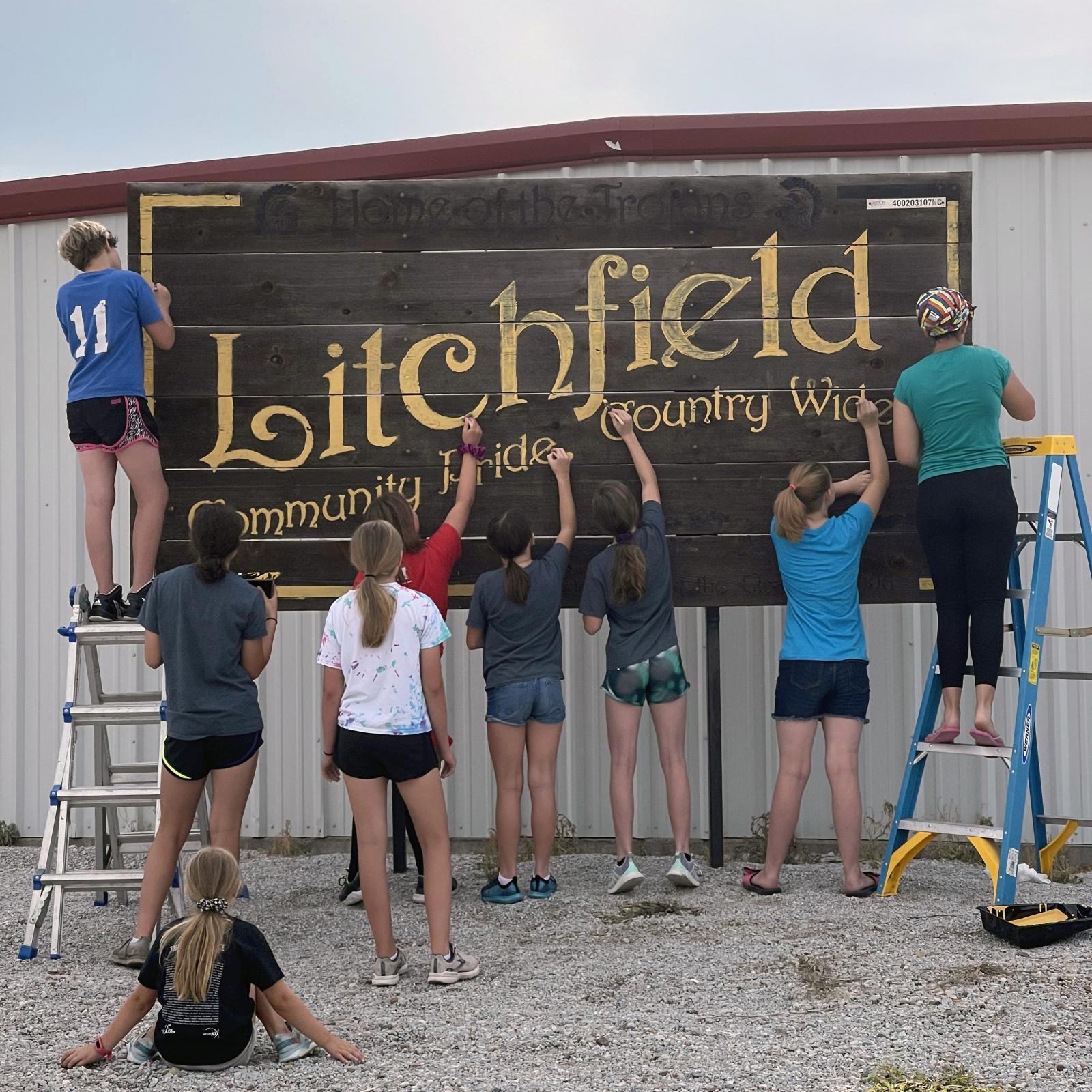 teenage 4-H club members work together to paint large "Litchfield" town sign