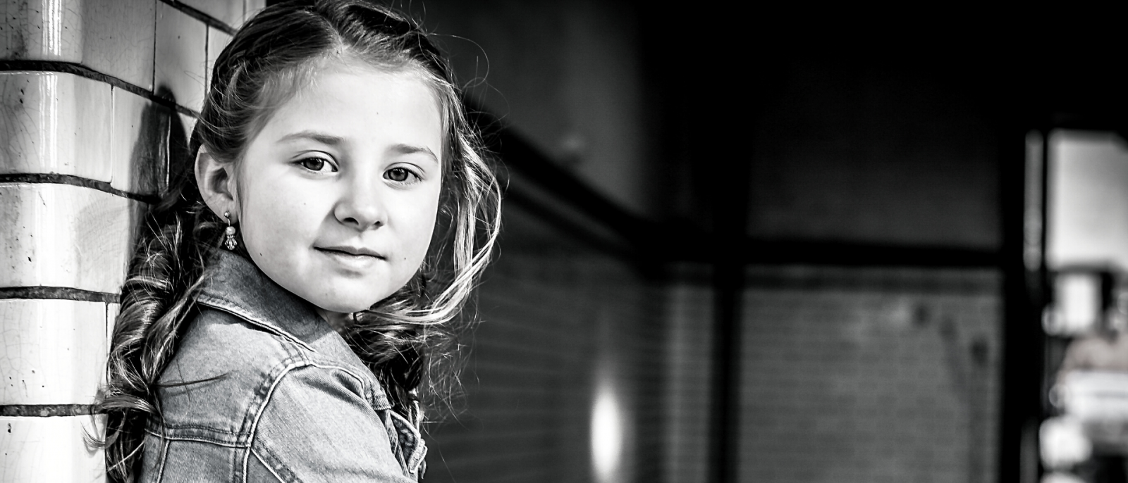 black and white photo of young girl leaning against a brick wall